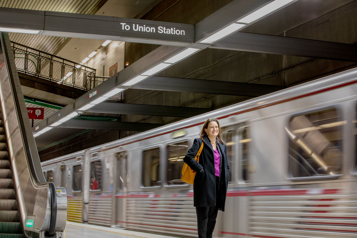 Katy Yaroslavsky stands in a subway station next to a moving train.